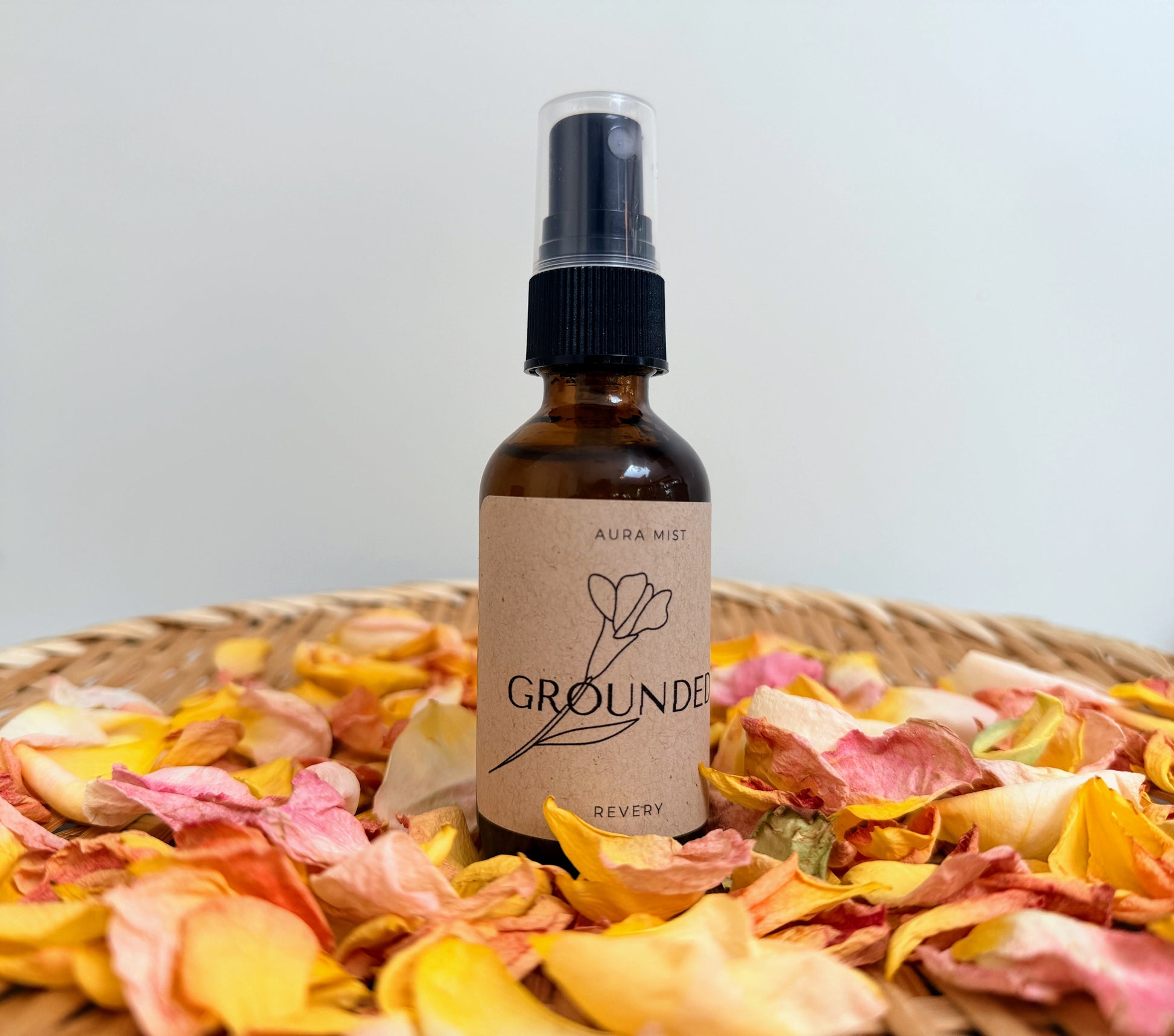 Bottle of 'Grounded' aspray on a bed of pink and yellow dried flowers with a plain background.