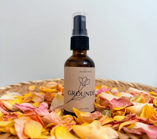 Bottle of 'Grounded' aspray on a bed of pink and yellow dried flowers with a plain background.